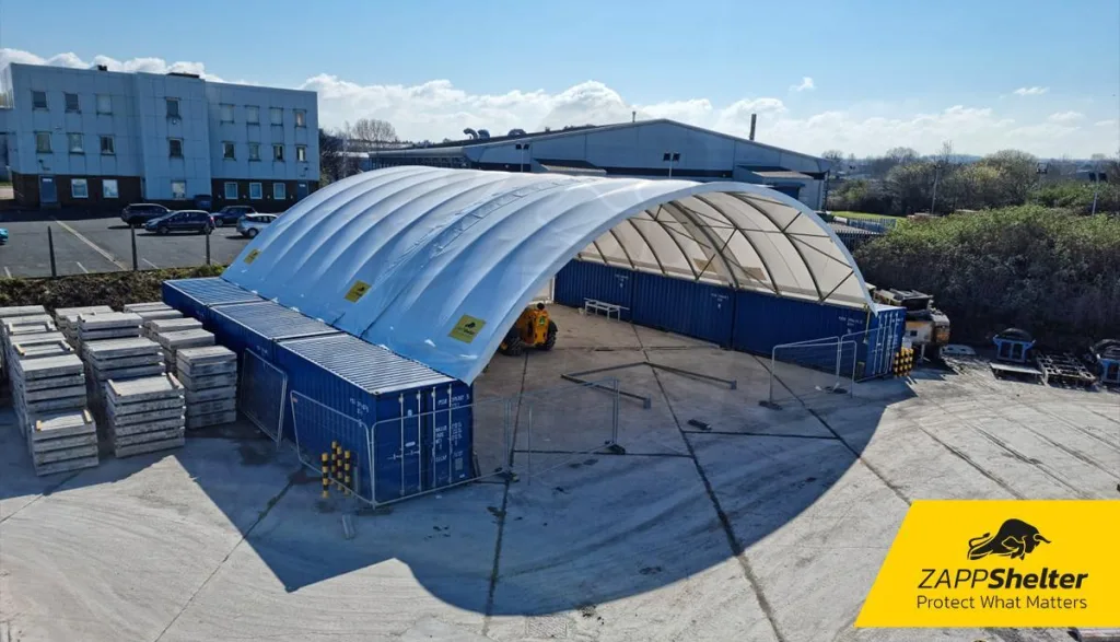 Wide-span Zappshelter fabric roof mounted on blue shipping containers in an industrial yard setting.